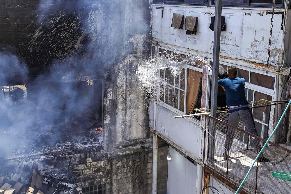 A man throws a bucket of water to dowse a fire in a building that was heavily damaged during an Israeli army raid on the Nur Shams camp. — AFP 