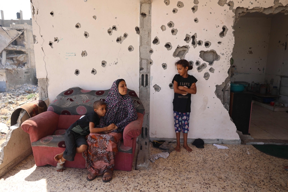 A Palestinian boy hugs a woman a she speaks to a girl while sitting on the balcony of a home damaged in Israeli bombardment, in Khan Yunis. — AFP 