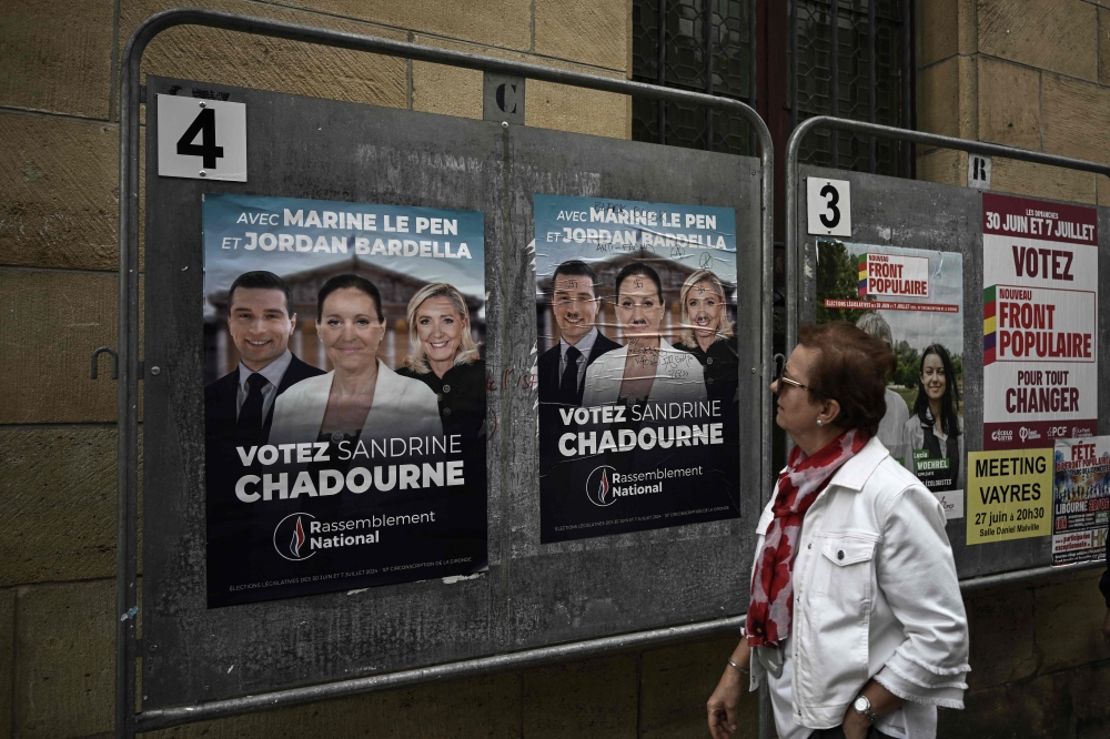 A woman looks at election posters of French far-right Rassemblement National (RN) candidate Sandrine Chadournec (C) in Libourne, southwestern France on July 2, 2024 as part of the French legislative elections. France's far right won the first round of pivotal legislative elections on June 30, 2024, with the centrist forces of France's President coming in only third behind the left after the highest turnout in over four decades. (Photo by Philippe LOPEZ / AFP)