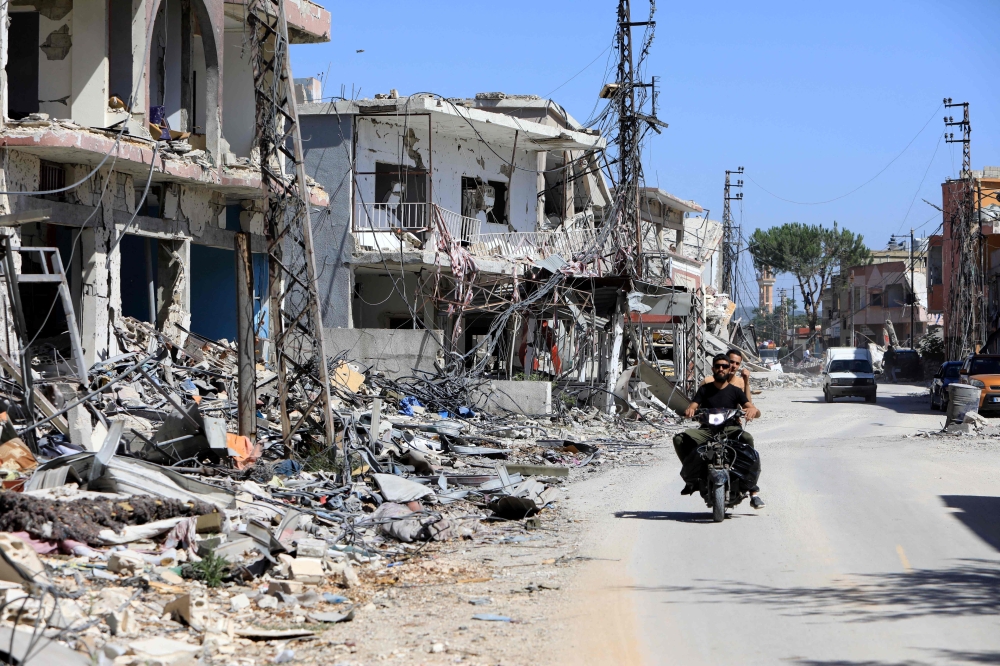 A motorbike drives past buildings destroyed during previous Israeli military fire on the southern Lebanese village of Aita al-Shaab, near the border with northern Israel on June 29, 2024, amid ongoing cross-border clashes between Israeli troops and Hezbollah fighters.  (Photo by AFP)

