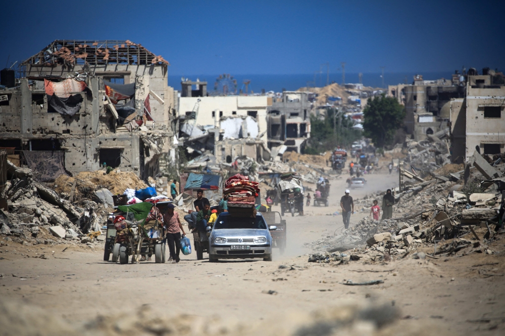 Palestinians walk and drive past buildings destroyed during previous Israeli bombardment, in Khan Yunis
