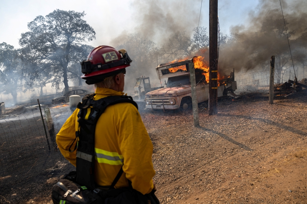 A firefighter looks at a vehicle on fire as he battles the Grubbs wildfire near Palermo, California. - Reuters
