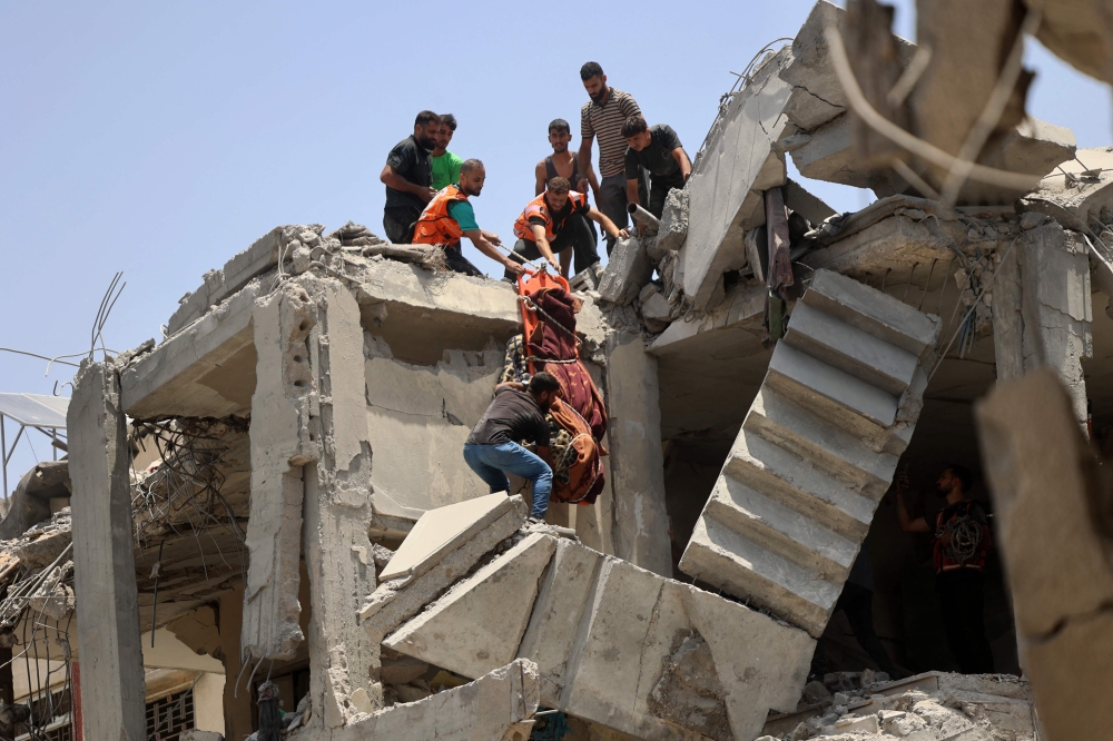 Rescuers lower the body of a person killed during the Israeli bombardment of a residential building situated next to the Great Omari Mosque in the Old City of Gaza City, which leads to damage historical Qaysariyya market and gold shops in Gaza City. - AFP

