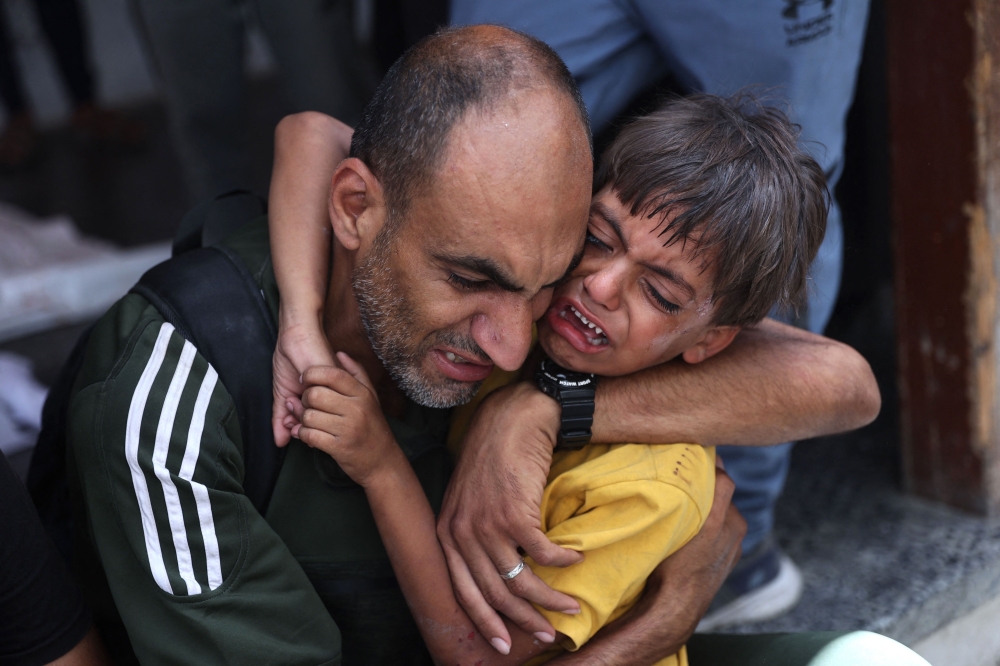 A Palestinian child is comforted as he stands near a bodybag (unseen) following Israeli bombardment of a Gaza City neighbourhood, at Al-Ahli Arab hospital, also known as the Baptist hospital in Gaza City on July 4, 2024, amid the ongoing conflict between Israel and the Palestinian Hamas militant group.  (Photo by Omar AL-QATTAA / AFP)