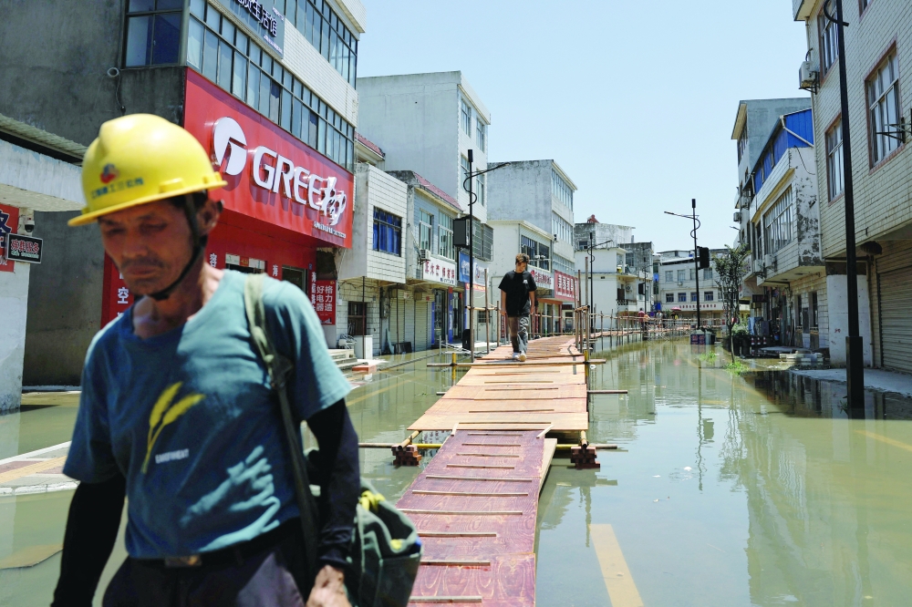 Residents cross a makeshift bridge after heavy rainfall and waters from the upstream Yangtze River flooded a town in Hukou county of Jiujiang, Jiangxi province. - Reuters
