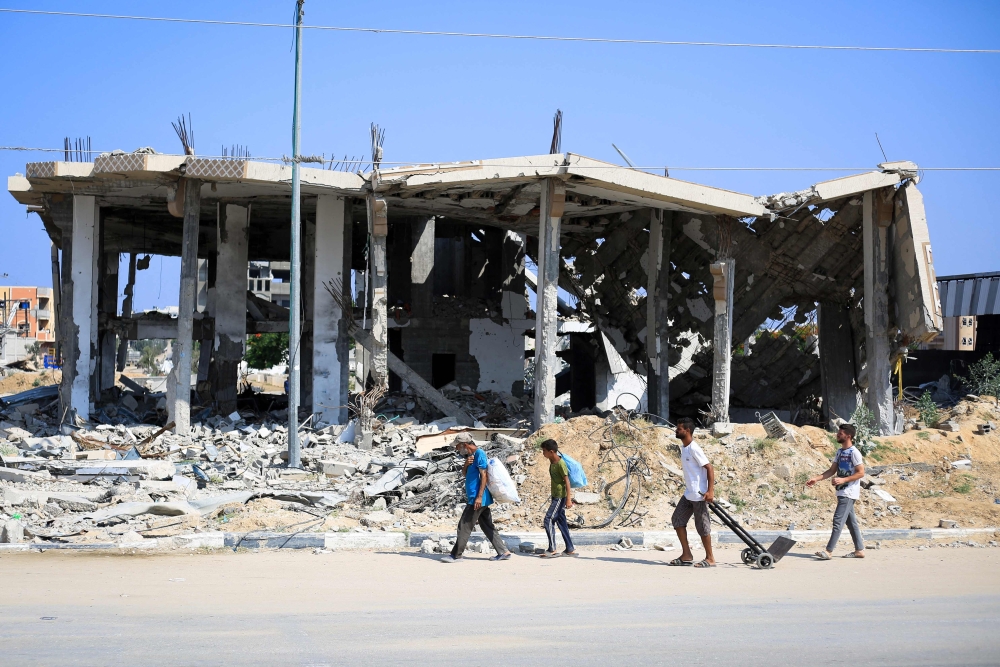 Displaced Palestinians carry belongings as they walk in front of a destroyed building in Deir el-Balah. — AFP 