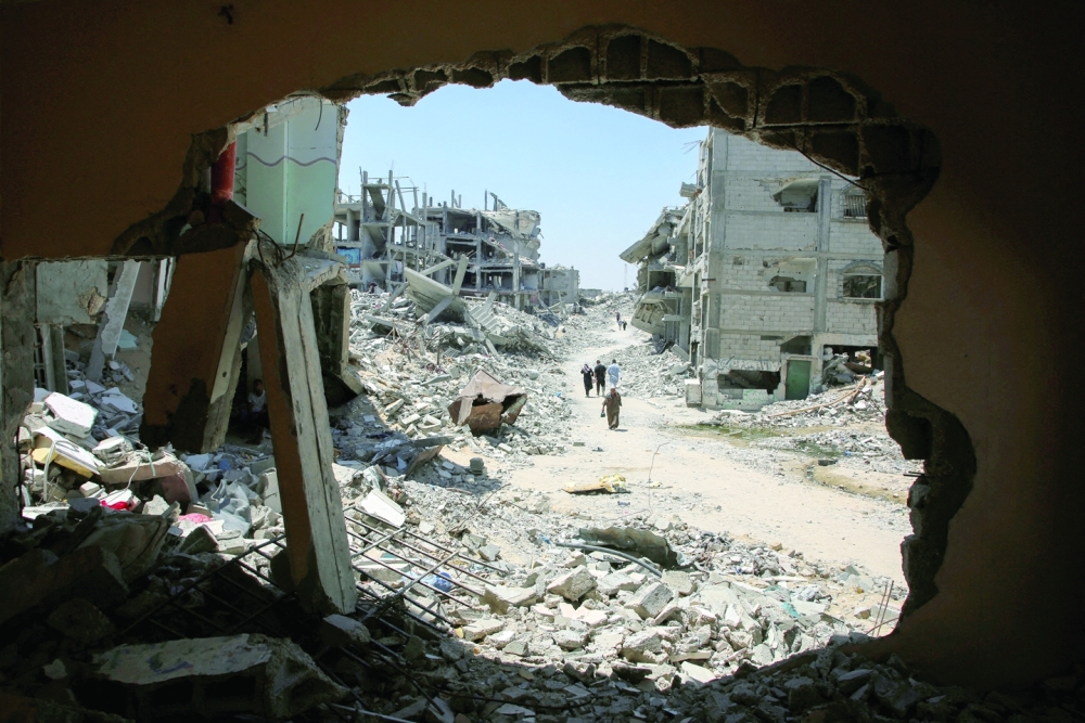 Palestinians walk past the rubble of houses destroyed during the Israeli military offensive, in Khan Younis. — Reuters 