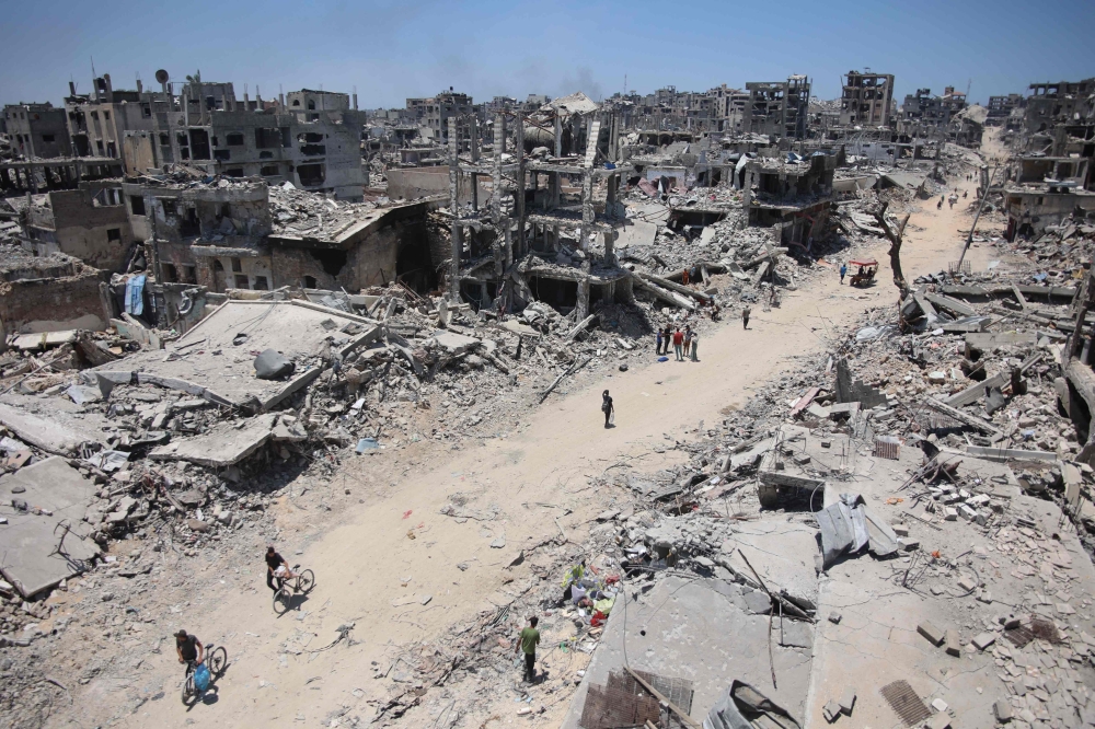 Palestinians walk along a road now dirt, past destoryed and razed buildings after the Israeli military withdrew following a two-week offensive from the Shujaiya neighbourhood, east of Gaza City on Thursday. — AFP