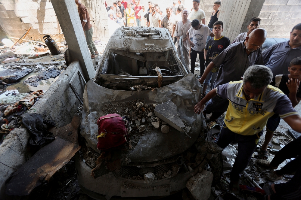 Palestinians gather to inspect a house hit in an Israeli strike, in Deir Al-Balah. — Reuters 