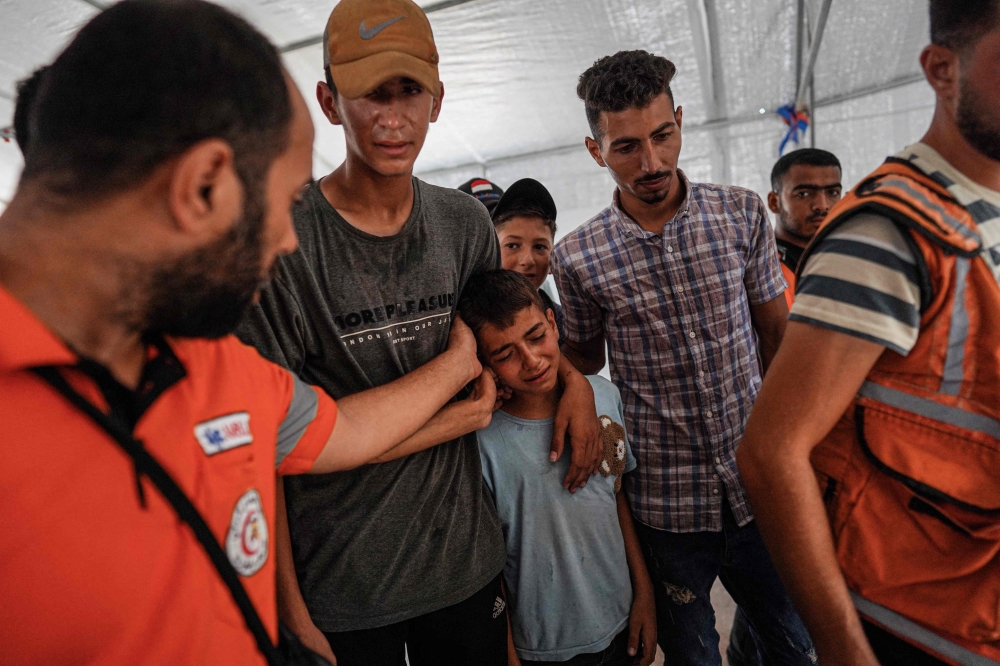 Relatives and Palestinian Civil Defence members comfort Ahmed, the son of their colleague Bilal Ramadan Farhan, 42, who died of injuries sustained in Israeli bombing of Al Mawasi area two days earlier, during his funeral at Nasser hospital in Khan Yunis. - AFP

