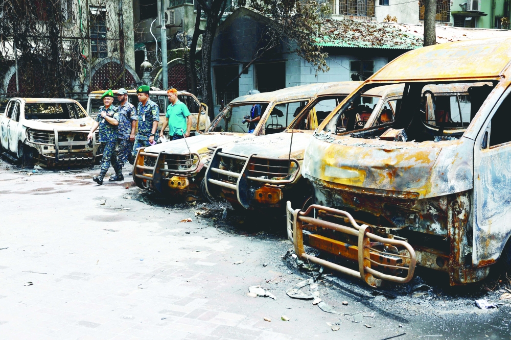 Security personnel walk past damaged vehicles of a government owned organization, in Dhaka. — Reuters 