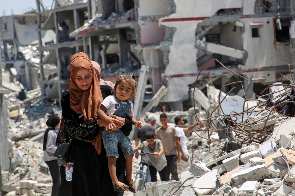 A Palestinian woman holds her daughter as she walks past the rubble of houses destroyed during the Israeli military offensive, amid Israel-Hamas conflict, in Khan Younis in the southern Gaza Strip. -  Reuters 
