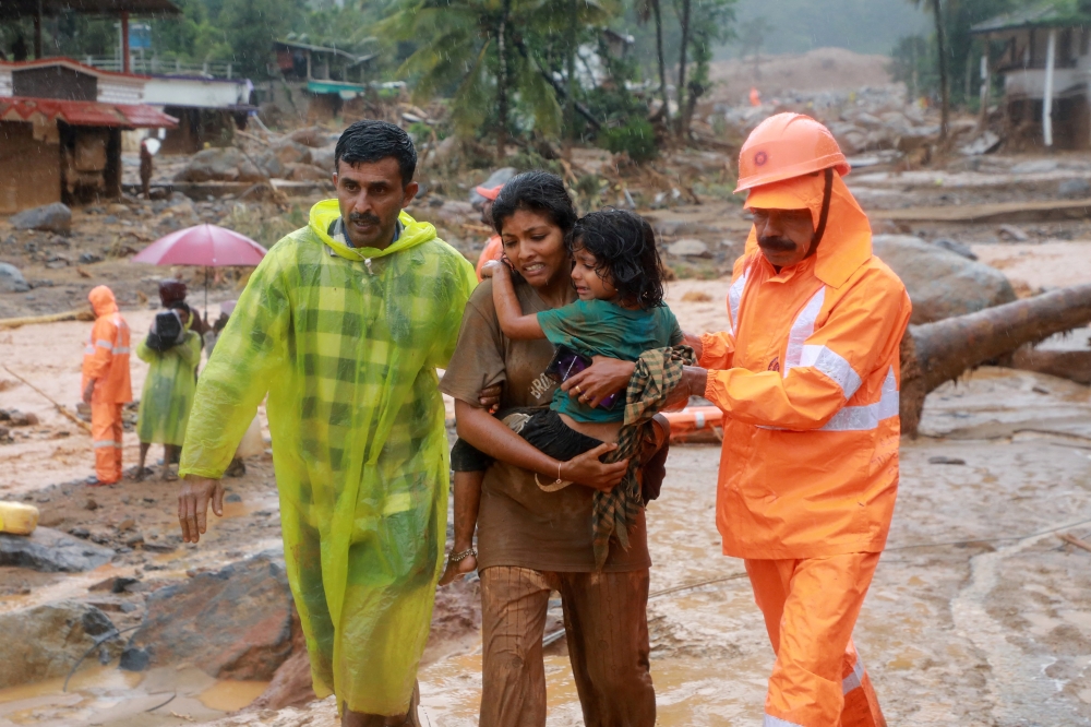Rescuers help residents to move to a safer place, at a landslide site after multiple landslides in the hills, in Wayanad