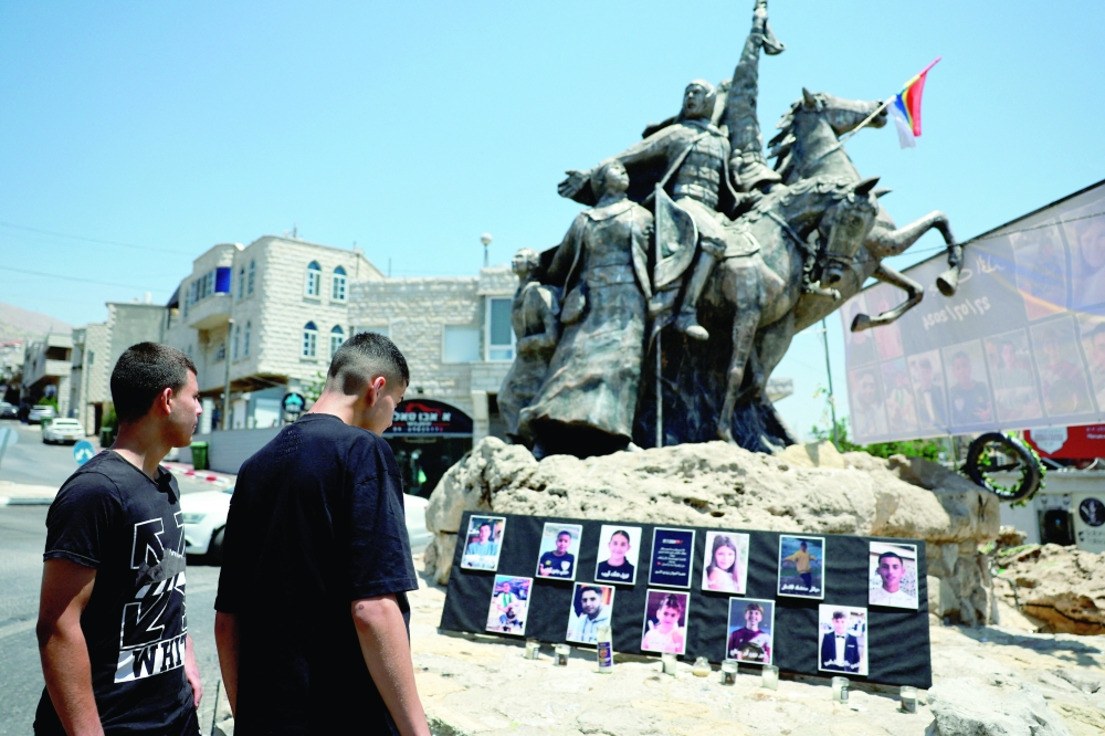 Young people look at the pictures of children and teens killed at a soccer pitch by a rocket Israel says was fired from Lebanon, at a roundabout in Majdal Shams on Monday. — Reuters