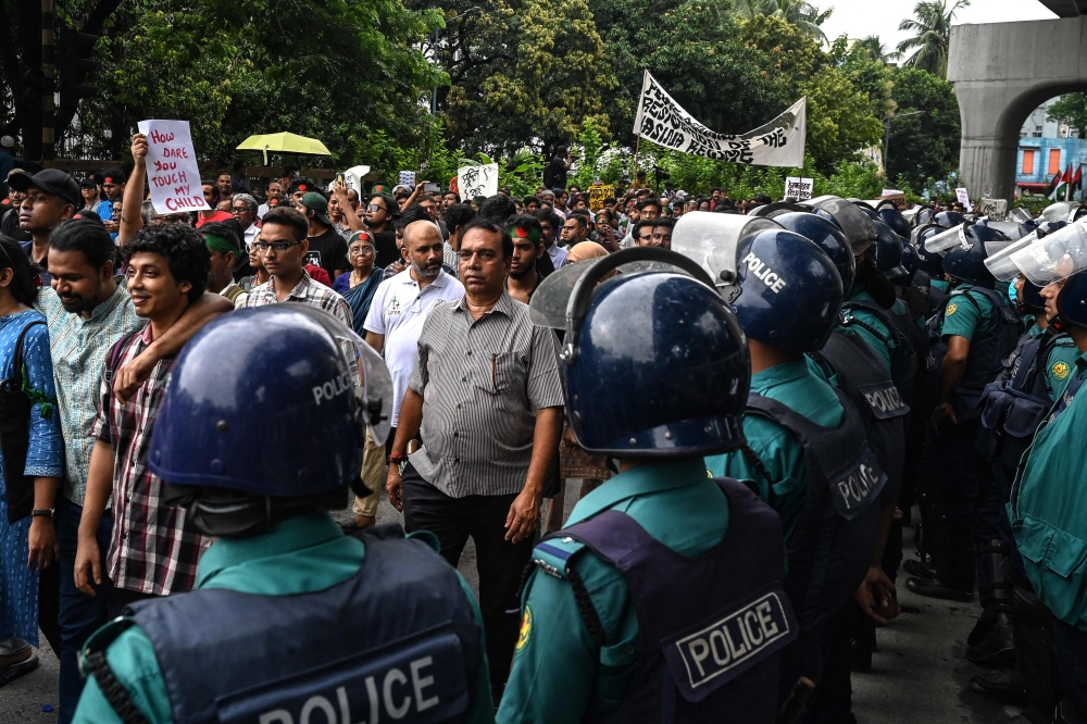 Activists walk past police personnel standing guard during a protest march demanding justice for victims arrested and killed in the recent countrywide violence in Dhaka