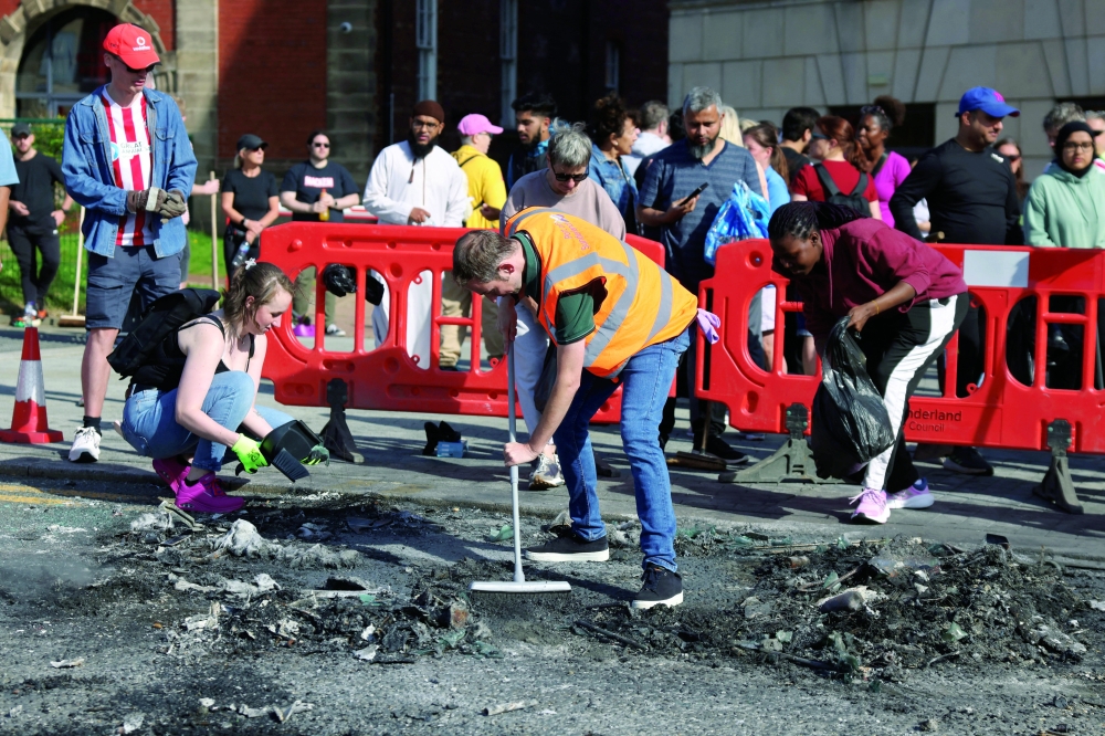 People help sweep up debris from a burnt vehicle after a night of violent anti-immigrant demonstrations, in Sunderland. - Reuters

