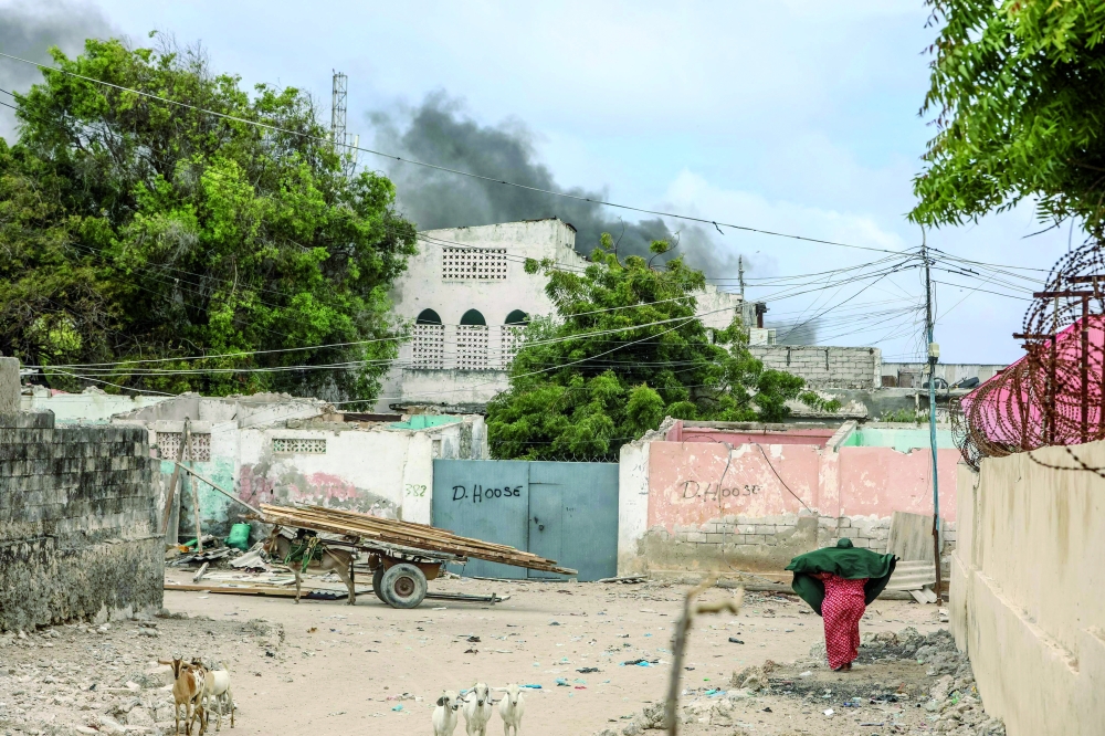 A woman reacts while walking in a street as smoke billows in the background from an explosive laden car diffused by the Somali police in Mogadishu. - AFP

