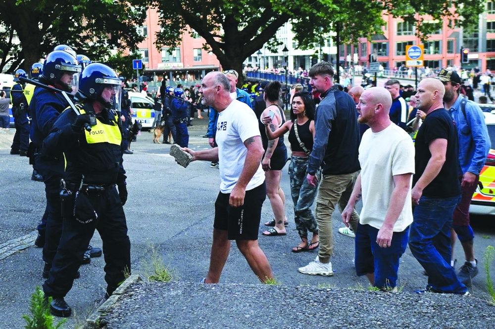 A protester holding a piece of concrete walks towards riot police as clashes erupt in Bristol. — AFP 