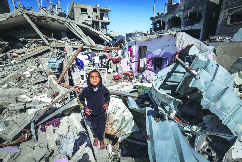 A Palestinian child looks up to watch a military drone as she stands on the rubble of destroyed houses in the Rafah refugee camp. — AFP file photo 