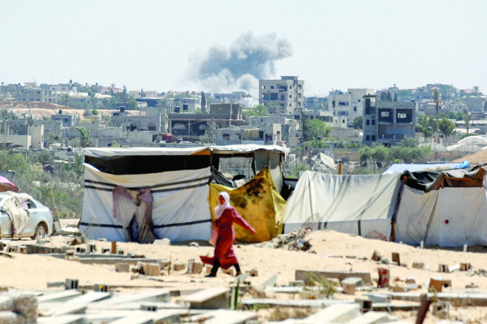 Smoke from Israeli bombardment billows in the background as a woman walks in Khan Yunis, Gaza. AFP 