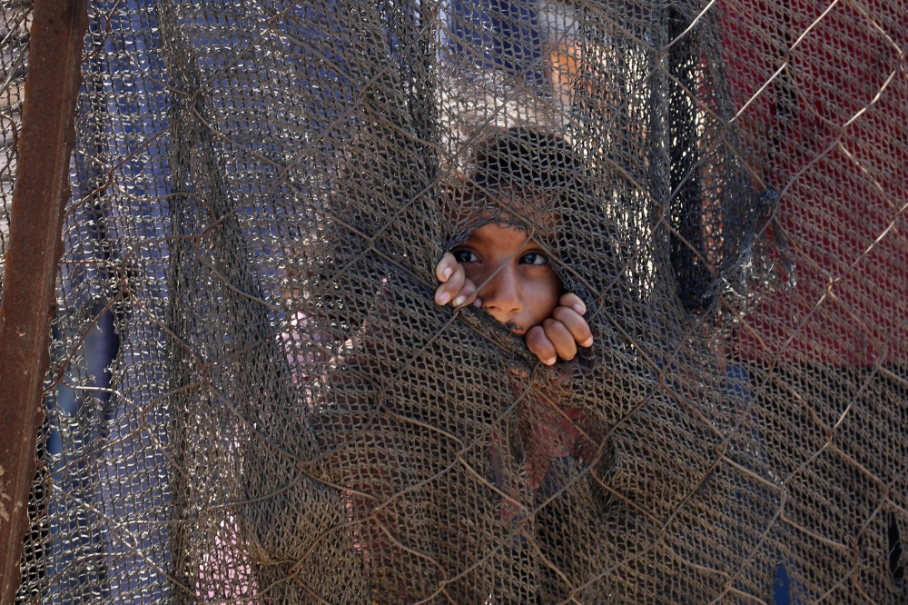 A displaced Palestinian child peeks through a hole in a fence in Deir el-Balah in the central Gaza Strip on Thursday. — AFP