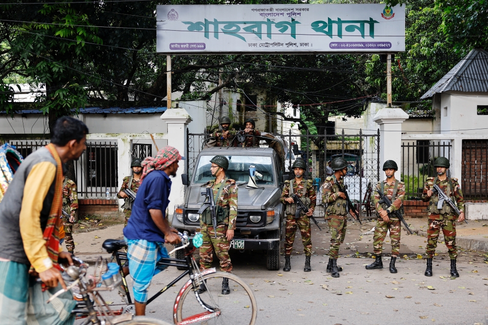 Rickshaw drivers pass army personnel standing guard in front of the Shahbagh Police Station, in Dhaka. — Reuters 