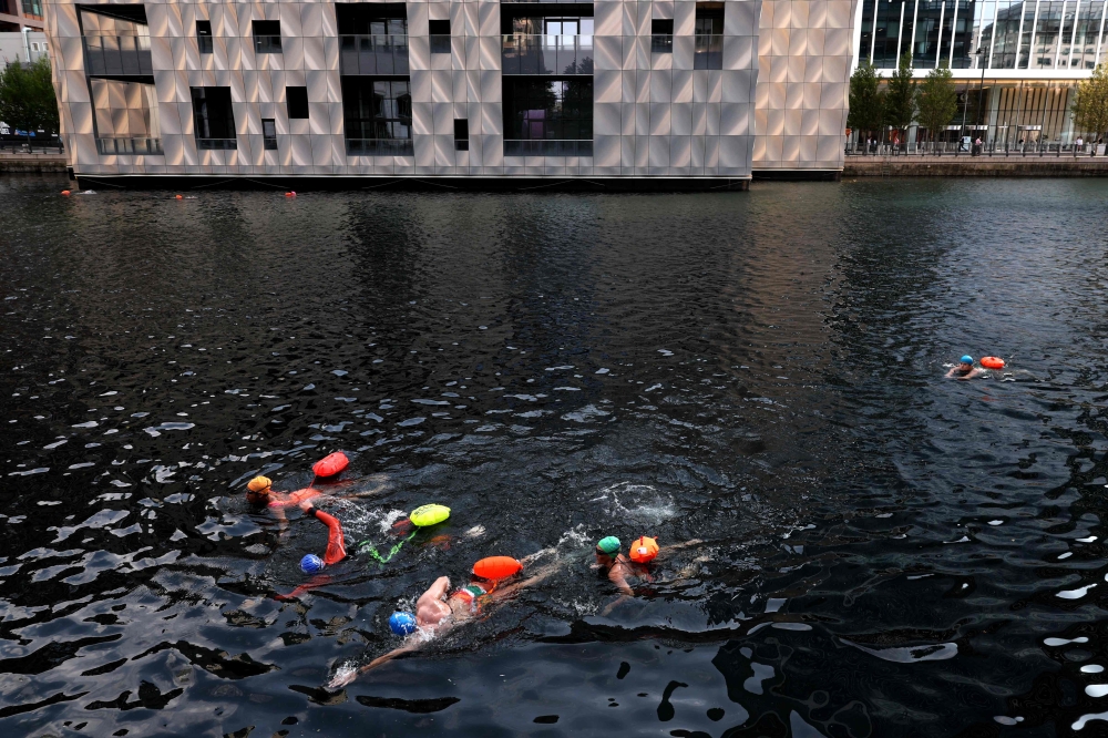 People swim in the Middle Dock of Canary Wharf in east London, on August 12, 2024, on what is set to be the hottest day of the year in the UK so far. (Photo by Adrian DENNIS / AFP)

