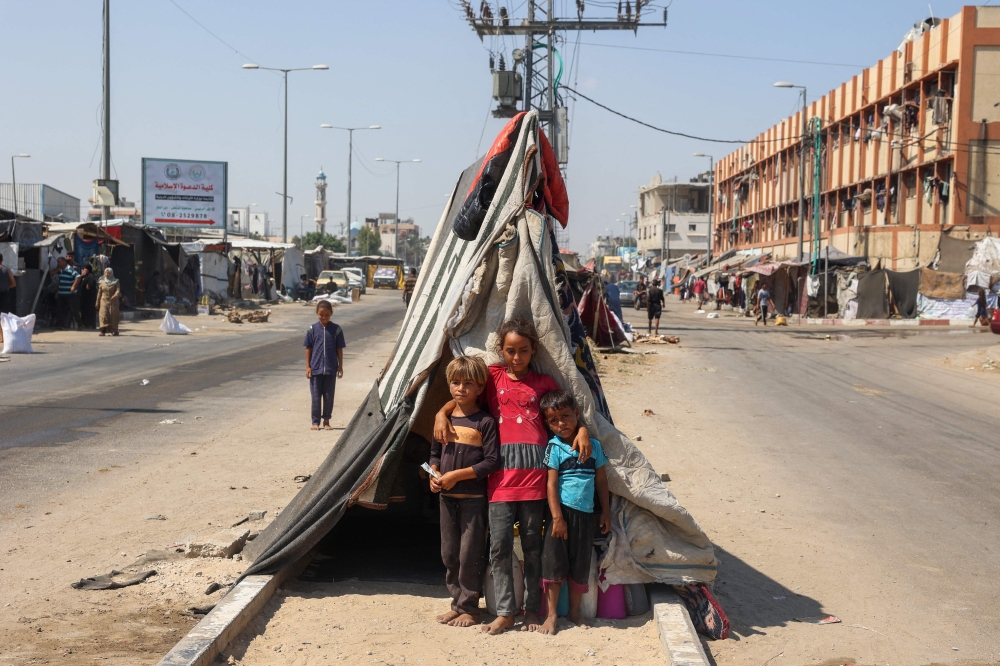 Palestinian children pose for a picture near their tent set on a road's median at a makeshift displacement camp set up along a road in Deir el-Balah. — AFP 
