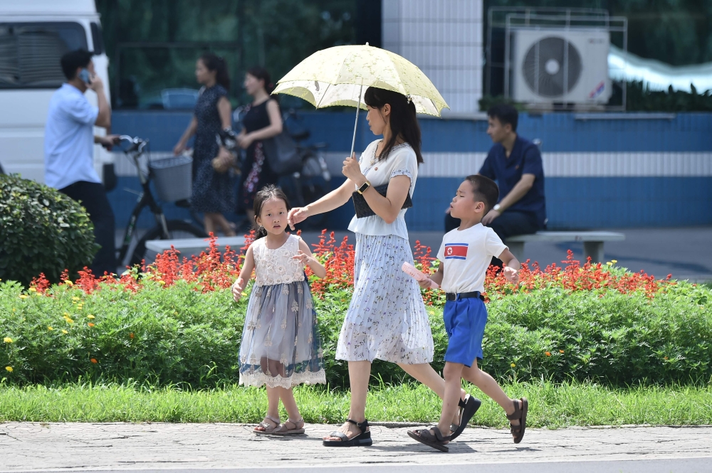 A woman uses an umbrella as she walks along the Mirae Scientists Street in Pyongyang during high temperatures o