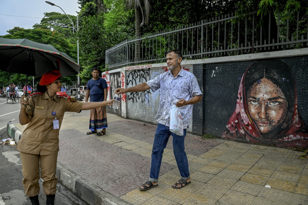 A father gives his daughter a water bottle while she manages traffic, in Dhaka, Bangladesh, on Aug. 11, 2024. (Atul Loke/The New York Times)