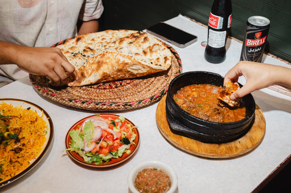 Patrons eat a variety of dishes  including rashoosh, a nigella-flecked flatbread baked in a clay oven  at Yemenat in Brooklyn, July 18, 2024. (Lanna Apisukh/The New York Times)