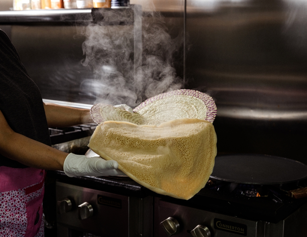 Master injera baker Gennet Wondimu removes a gluten-free ivory injera from the pan at Ye Geny Injera & Mini Market in Inglewood