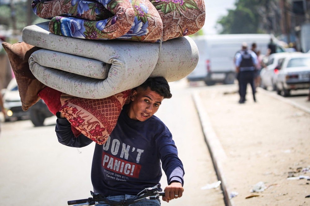 A young man riding a bicycle carries bedding on his shoulder as Palestinians flee with their belongings Deir el-Balah in the central Gaza Strip