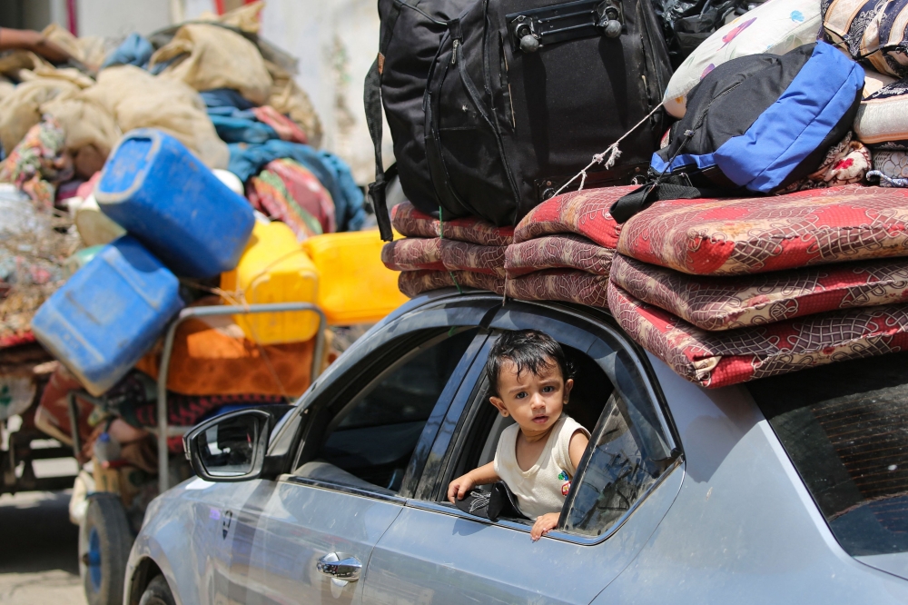 A child peeks out from the window of a car as Palestinians flee with their belongings Deir el-Balah