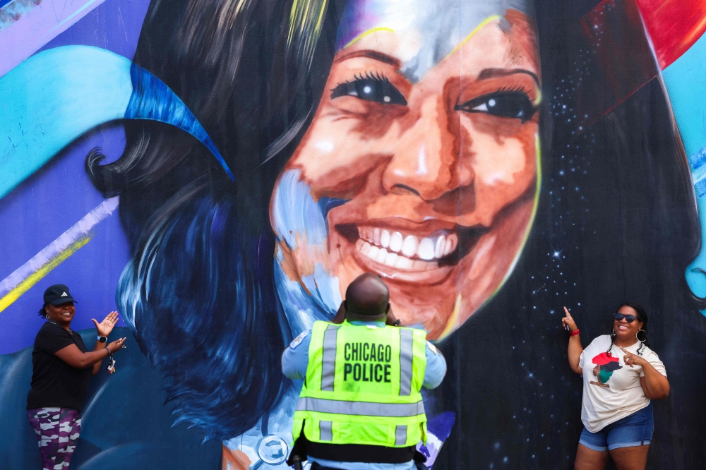 A police officer takes a picture of people posing before a mural of US Vice-President Kamala Harris outside the United Center 