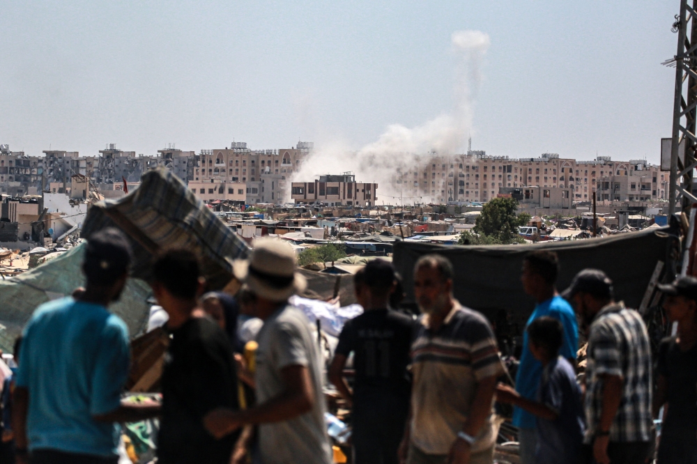 Displaced Palestinians watch as shells fired from Israeli tanks hit 