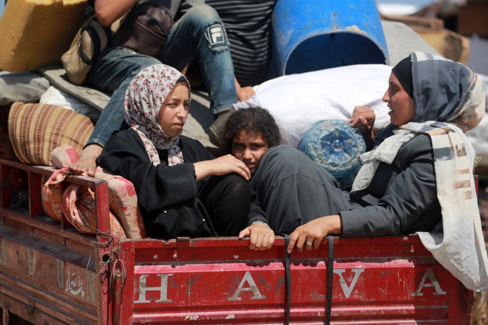 Palestinians sit atop their belongings in the back of a vehicle as they flee a makeshift camp for displaced people in Khan Yunis