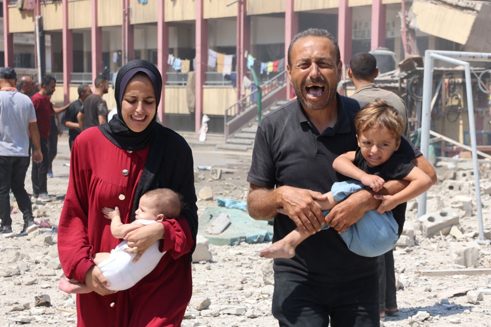 Palestinians carry their children as they flee after an Israeli strike on a school, housing displaced Palestinians, in the Rimal neighbourhood of central Gaza City on August 20, 2024, amid the ongoing conflict between Israel and the militant Hamas group.  (Photo by Omar AL-QATTAA / AFP)
