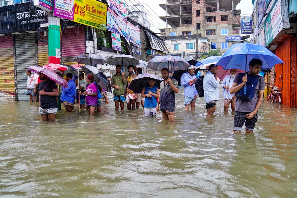 People carrying umbrellas, wade through a flooded street amid rainfall in Feni. - AFP
