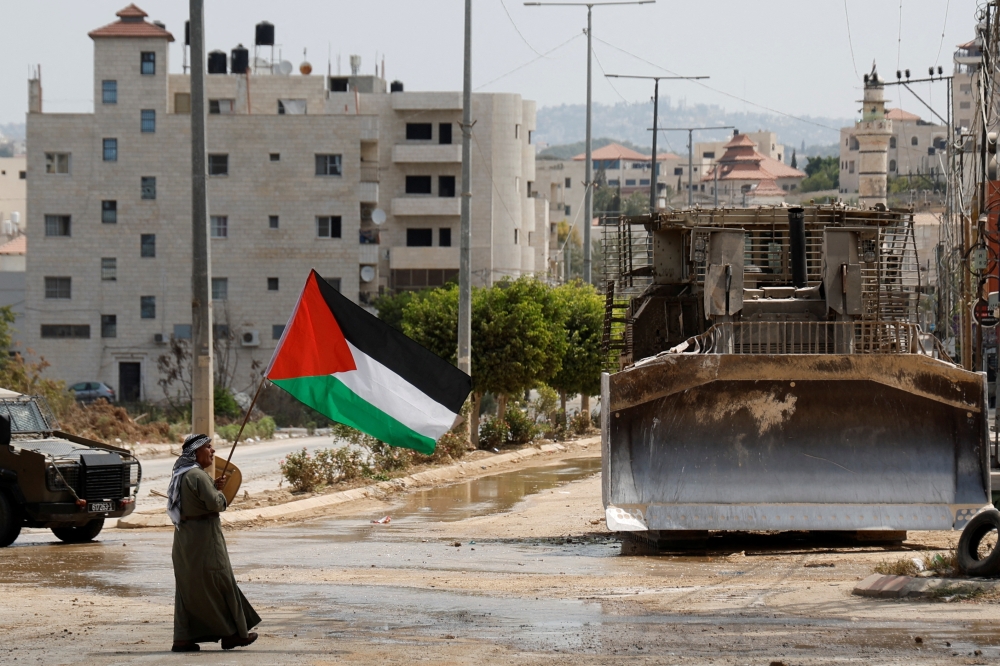 A man holds the Palestinian flag next to an Israeli military bulldozer during a raid in Tulkarm, in the Israeli-occupied West Bank, on Thursday. - Reuters