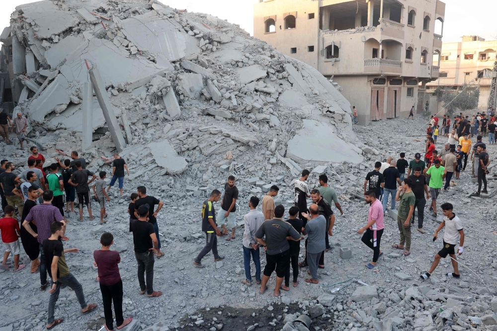 Palestinians gather to check a building shortly after it was leveled by Israeli bombing in the Nuseirat refugee camp