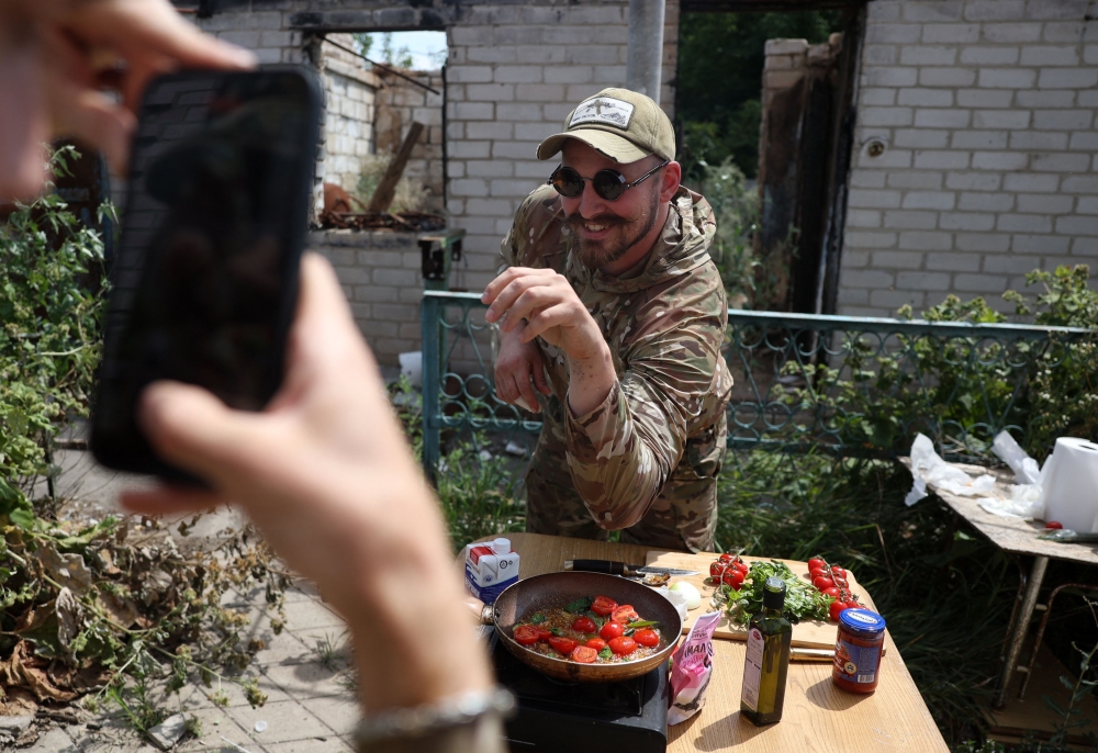 Ukrainian serviceman and influencer Ruslan Mokrytskyi poses for the camera as he cooks pasta as his fellow soldier records a video of him for Tik Tok  