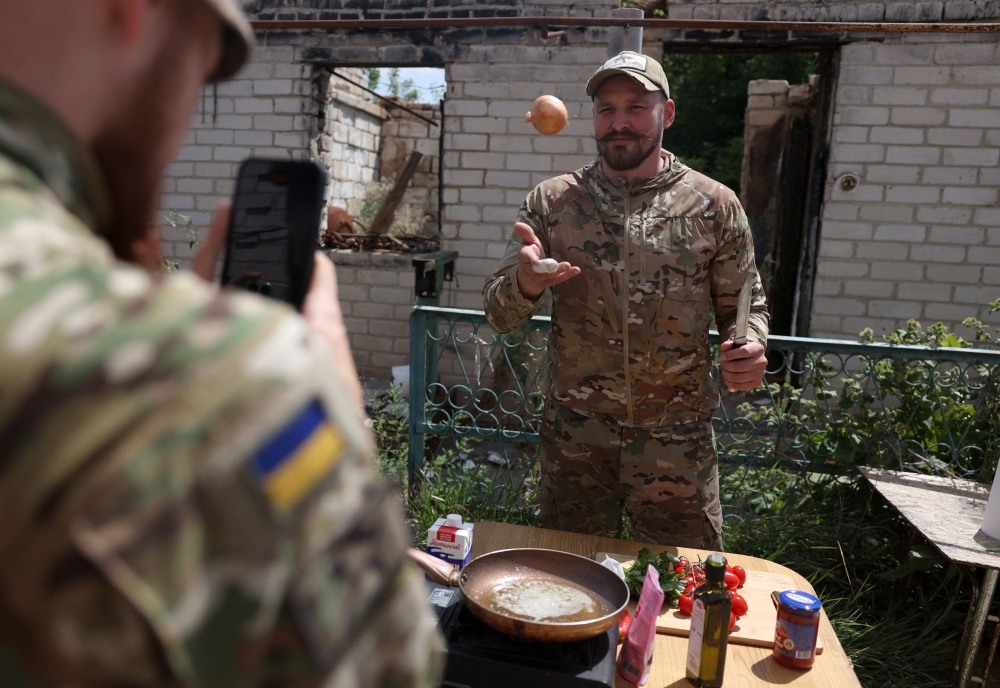 Ukrainian serviceman and influencer Ruslan Mokrytskyi cooks pasta as his fellow soldier records video of him for Tik Tok in the Donetsk region 