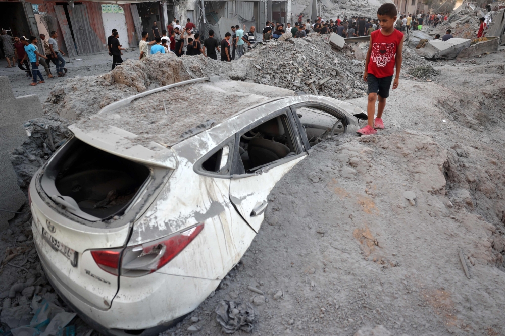 A young Palestinian boy stands near a car buried in rubble in the vicinity of a building shortly after it was levelled by Israeli bombing