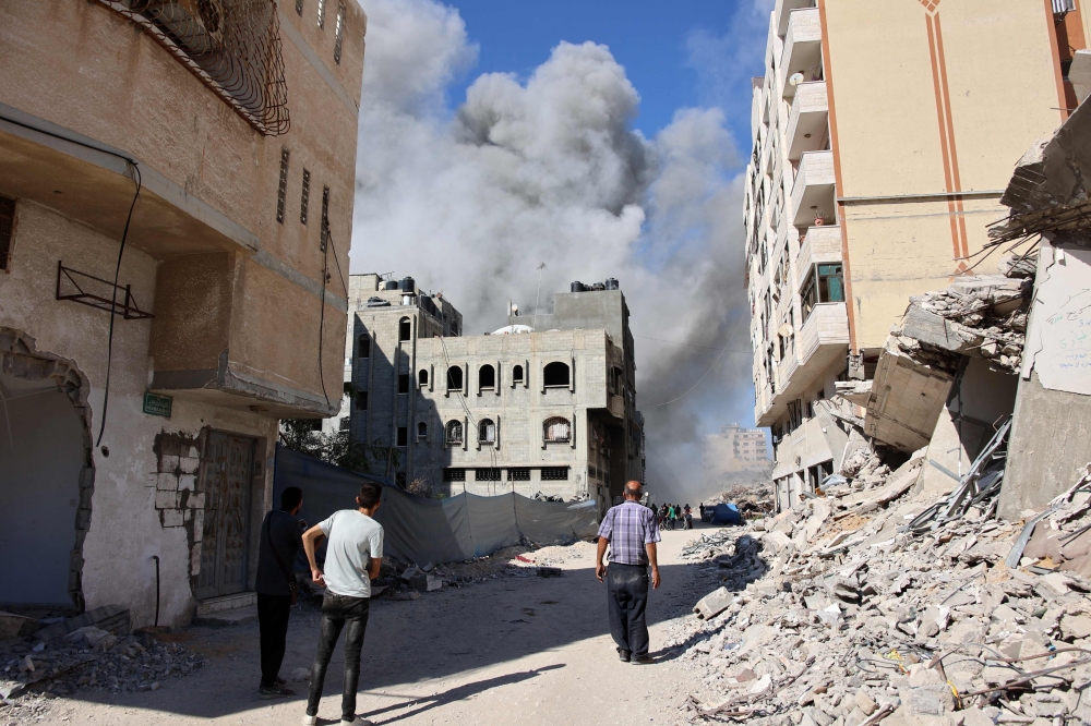 Palestinians watch as smoke rises from a building hit by an Israeli strike after a warning from the army to its occupants to evacuate the premises