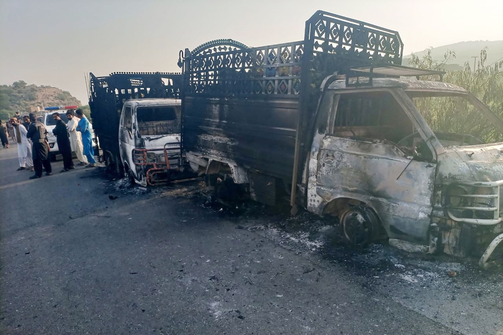Security personnel stand near the charred vehicles at the shooting site on the national highway in Musakhail district. — AFP 