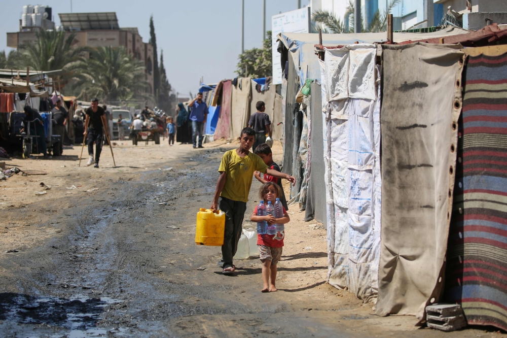 Displaced Palestinian children haul water to their tent in a makeshift camp in the perimeter of the Al-Aqsa Martyrs Hospital. — AFP 