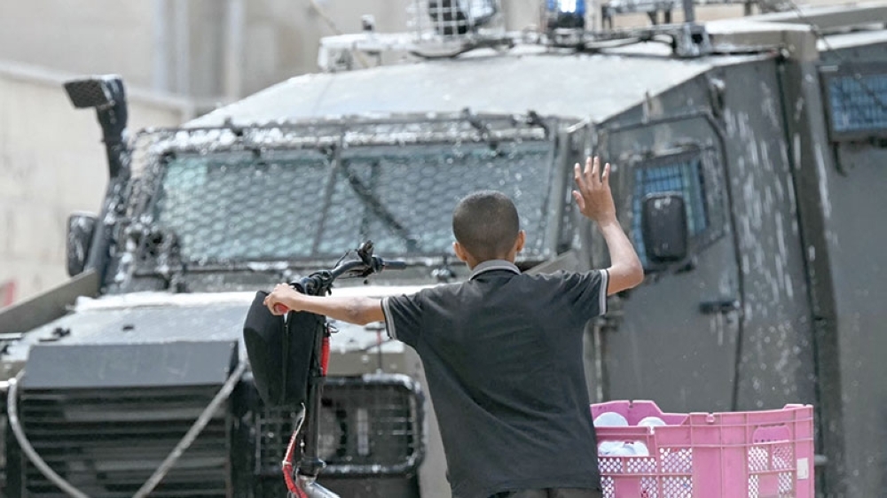 A Palestinian boy rises his hand into the air as Israeli soldiers inspect what he is carrying during a raid in Jenin in the occupied West Bank on Wednesday. - AFP