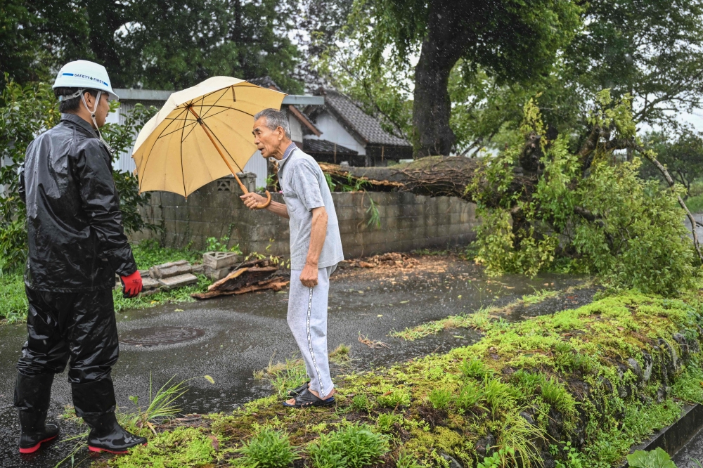People chat next to a fallen tree brought down by strong winds from Typhoon Shanshan in Usa, Oita prefecture on August 29, 2024. Typhoon Shanshan hit Japan with full force on August 29, injuring dozens as howling winds smashed windows and blew tiles off houses while torrential rains turned rivers into raging torrents. (Photo by Yuichi YAMAZAKI / AFP)