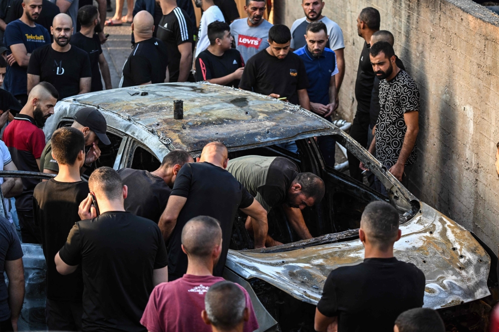 People check a burnt car in the small town of Zababdeh, southeast of Jenin in the occupied West Bank